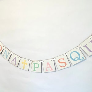 May include: A white banner with the words "BUONA PASQUA" in pastel colors. The letters are on individual squares with a white background and are connected by white string.