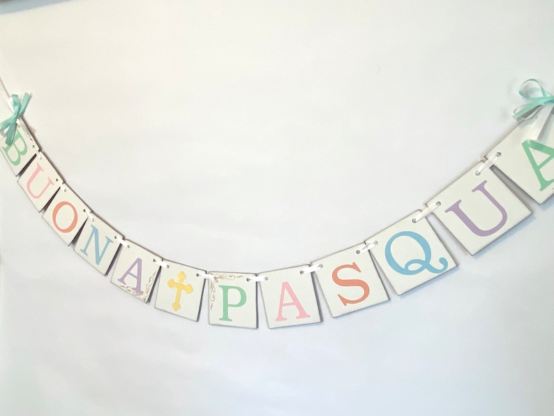 May include: A white banner with the words "BUONA PASQUA" in pastel colors. The letters are on individual squares with a white background and are connected by white string.