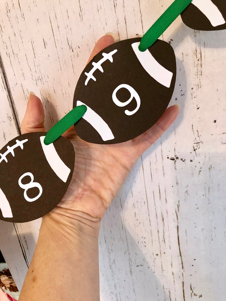 May include: A green and brown football-shaped banner with the numbers 8 and 9 printed on it. The banner is made of paper and has a white string running through it.