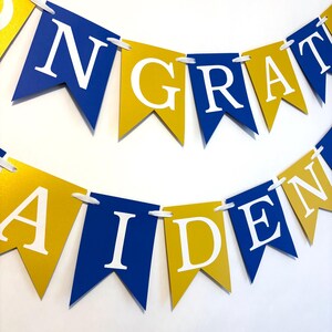 May include: A blue and gold banner with the words "CONGRATULATIONS" and "AIDEN" in white letters.