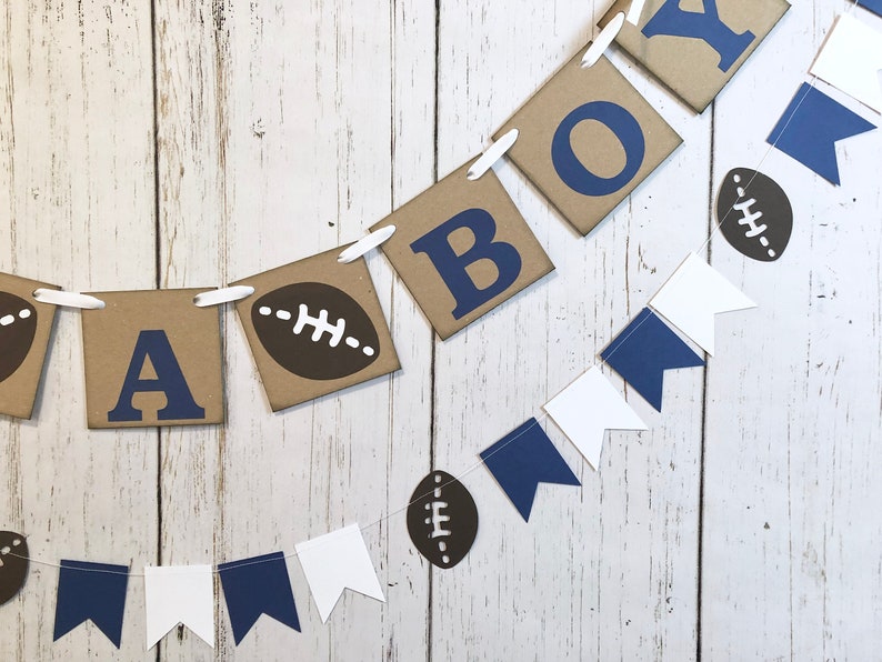 May include: A brown and white banner with the word "BOY" in blue letters, decorated with brown footballs and blue and white pennants.
