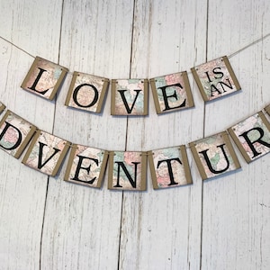 May include: A banner with the words "LOVE IS AN ADVENTURE" printed on individual flags. Each flag has a vintage world map design with a brown background.