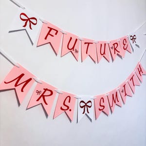 May include: Two banners with pink and white pennants. The top banner reads "FUTURE" in red script, and the bottom banner reads "MRS SMITH". Each pennant has a red bow graphic. The banners are strung on white string.