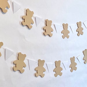May include: A brown teddy bear banner with white triangle flags. The banner is strung together with white string. The teddy bears are cut out of brown paper and are all the same size.