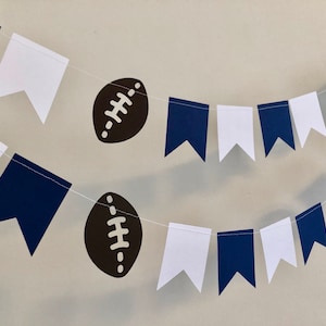 May include: A navy blue and white bunting with brown footballs. The bunting is strung together with white string.