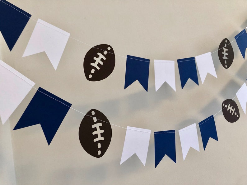 May include: A navy blue and white bunting with brown footballs. The bunting is strung together with white string.