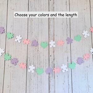 May include: A garland of pastel colored puzzle pieces in white, light green, light pink, and lavender. The garland is strung together with a white string. The text "Choose your colors and the length" is written above the garland.