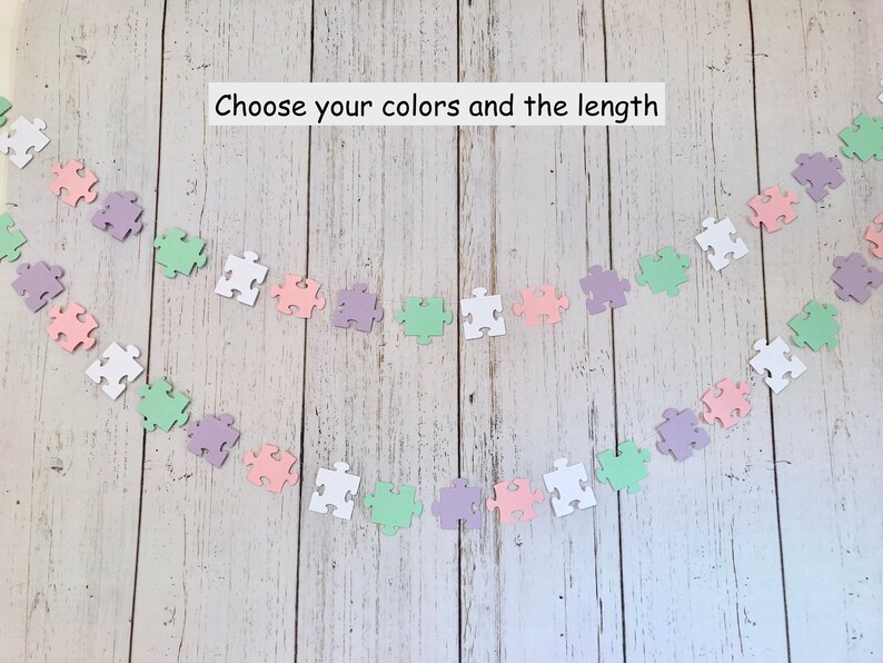 May include: A garland of pastel colored puzzle pieces in white, light green, light pink, and lavender. The garland is strung together with a white string. The text "Choose your colors and the length" is written above the garland.