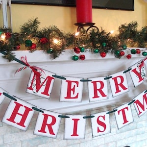 May include: A white and red Christmas banner with the words "Merry Christmas" hanging on a white fireplace mantel. The banner is decorated with green garland and red and green ornaments.