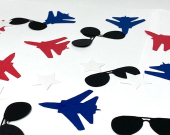 May include: A collection of blue, red, and black paper cutouts of fighter jets and sunglasses. The cutouts are scattered on a white surface.