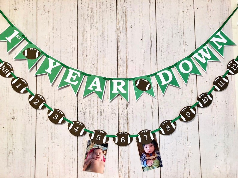 May include: Green and white banner with the text "1st Year Down" and a string of brown and white football-shaped decorations with numbers 1 through 12. Two photos are attached to the footballs.