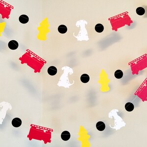 May include: A red, white and black paper garland featuring fire engines, dalmatian dogs and fire hydrants. The garland is strung together with black circles.