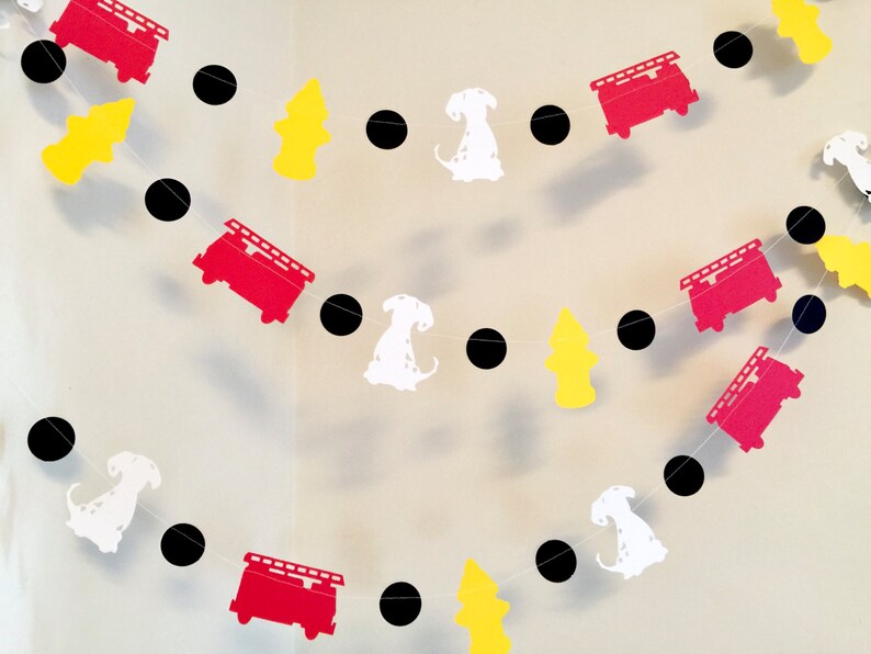 May include: A red, white and black paper garland featuring fire engines, dalmatian dogs and fire hydrants. The garland is strung together with black circles.