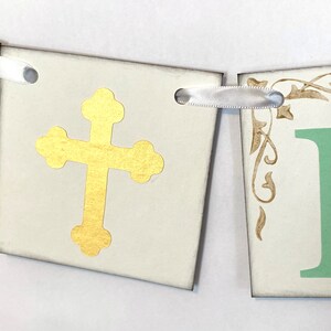May include: A white banner with gold cross and green letter "F" on each of the two sections. The banner is decorated with gold floral designs and has white ribbon ties.