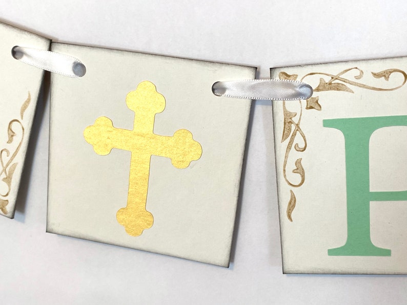 May include: A white banner with gold cross and green letter "F" on each of the two sections. The banner is decorated with gold floral designs and has white ribbon ties.