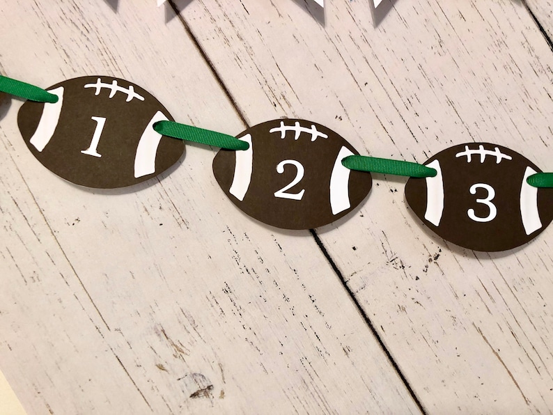 May include: A brown and white football-shaped banner with the numbers 1, 2, and 3 printed on it. The banner is strung together with green ribbon.
