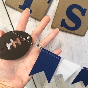 May include: A navy blue and white pennant banner with a brown football cutout. The banner has the words "It's" on it.