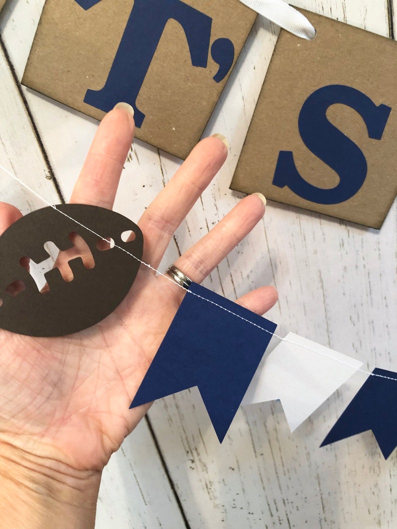 May include: A navy blue and white pennant banner with a brown football cutout. The banner has the words "It's" on it.