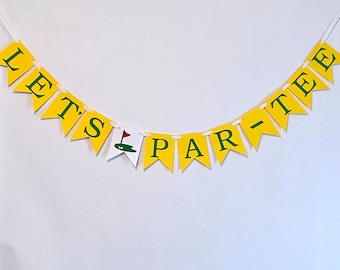 May include: A yellow and green banner with the text "Let's Par-Tee" in white letters. The banner is strung together with white string and has a small green golf flag icon in the center.