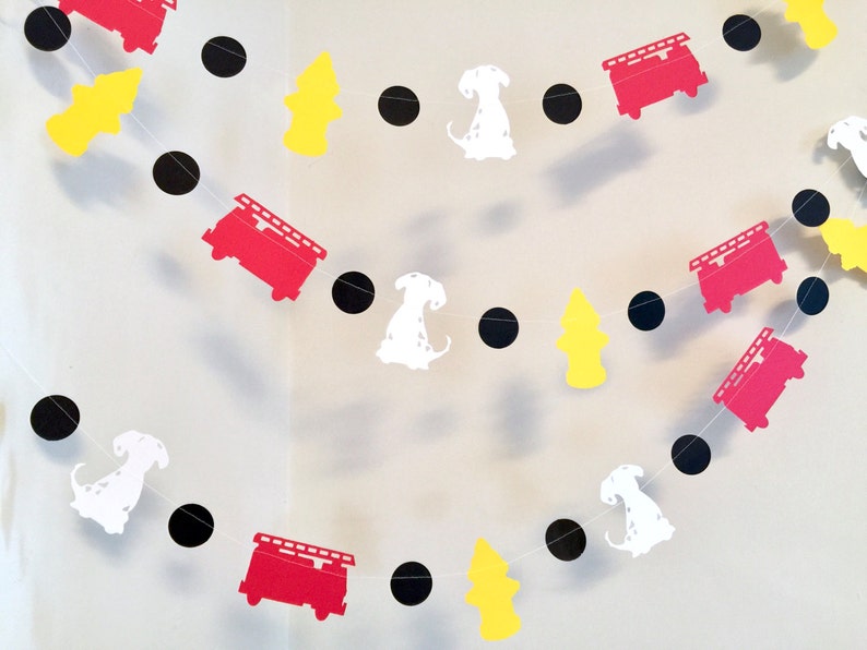 May include: A red, white and black paper garland featuring fire engines, dalmatian dogs and fire hydrants. The garland is strung together with black circles.