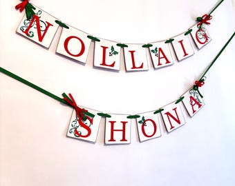 May include: A white banner with red letters spelling "Nollaig Shona" with green holly accents and red bows.