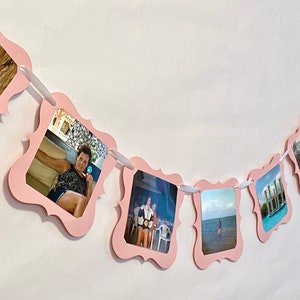 May include: Pink photo banner with white ribbon and photos of people and places. The banner is made of paper and has a scalloped edge.