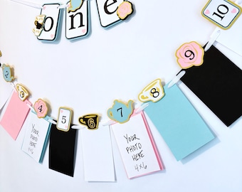 May include: A decorative photo banner with the word "one" and numbers 2-10. The banner includes photo holders in pink, black, white, and blue. Each photo holder is 4x6 inches. The banner is decorated with teacups, teapots, and roses.