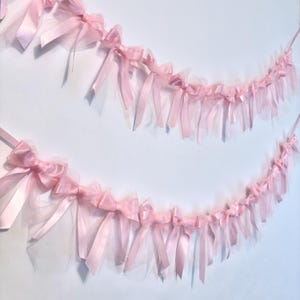 May include: A pink tulle and satin ribbon garland with bows. The garland is strung together with a white string and is perfect for a party or special occasion.
