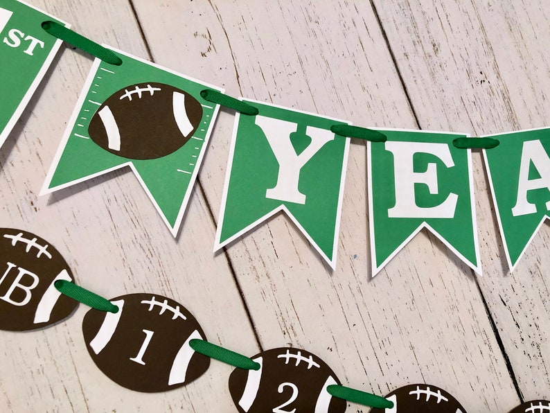 May include: Green and white banner with the words "First Year" and football graphics. The banner is strung with green ribbon.