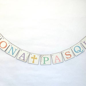 May include: A white banner with the words "BUONA PASQUA" in colorful letters. The letters are on individual squares with a gold cross in between the words.