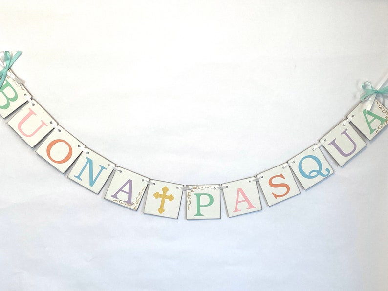 May include: A white banner with the words "BUONA PASQUA" in colorful letters. The letters are on individual squares with a gold cross in between the words.
