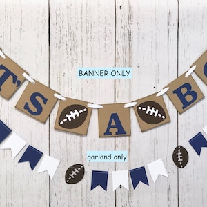 May include: It's a boy banner with brown paper squares with blue letters and footballs. A matching garland with blue and white pennants and footballs.