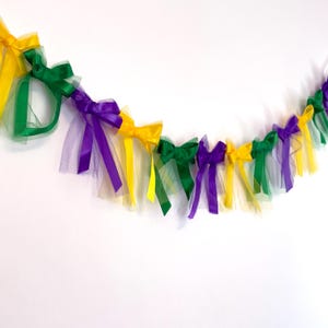 May include: A Mardi Gras garland with purple, green, and gold bows and tulle. The garland is perfect for decorating for a Mardi Gras party.