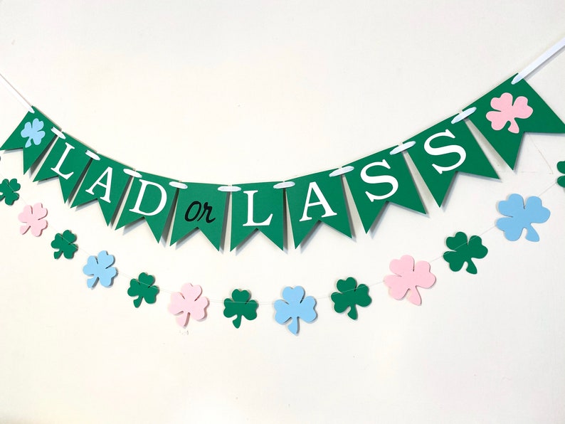 Pu&ograve; includere: Uno striscione verde e bianco con il testo "Lad or Lass" e una stringa di trifogli verdi, rosa e blu.