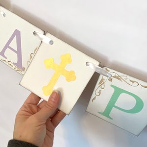May include: A white banner with the word "Happy" in purple, a gold cross, and the letter "P" in green. The banner is strung together with white ribbon.