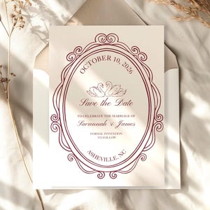 May include: A cream-colored wedding invitation with burgundy text and a decorative oval frame. The text reads "October 10, 2026," "Save the Date," and the names "Savannah & James." The invitation is inside a cream envelope.