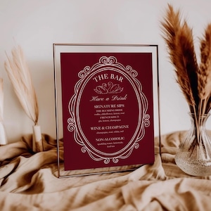 May include: A burgundy bar menu sign in a clear frame. The sign features white text with a decorative oval border, listing drink options like signature sips, wine, champagne, and non-alcoholic beverages.