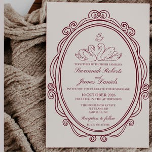 May include: Wedding invitation with a burgundy frame and swan illustration. The invitation includes the names Savannah Roberts and James Daniels, the date October 10, 2026, and the dress code, Black Tie Attire.