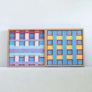 Könnte beinhalten: Zwei quadratische Holzrahmen mit gewebter Faser-Kunst. Der linke Rahmen zeigt horizontale und vertikale Streifen in Rot, Weiß, Blau und Lila. Der rechte Rahmen zeigt ein Gittermuster aus leuchtend gelbem und blauem Garn mit roten Akzenten.