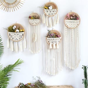 May include: Five circular wall hangings featuring woven rattan baskets with cream-coloured macrame pockets. Each basket contains dried flowers and cotton bolls. Long, cream-coloured macrame fringe and tassels hang from the bottom of each basket.