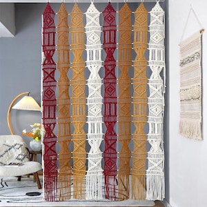 May include: A macrame curtain with alternating vertical panels of burgundy, cream, and mustard yellow. The curtain is hung from a white track and features geometric patterns and fringe at the bottom. The text "LIBRE VOYAGE" is visible at the bottom right.