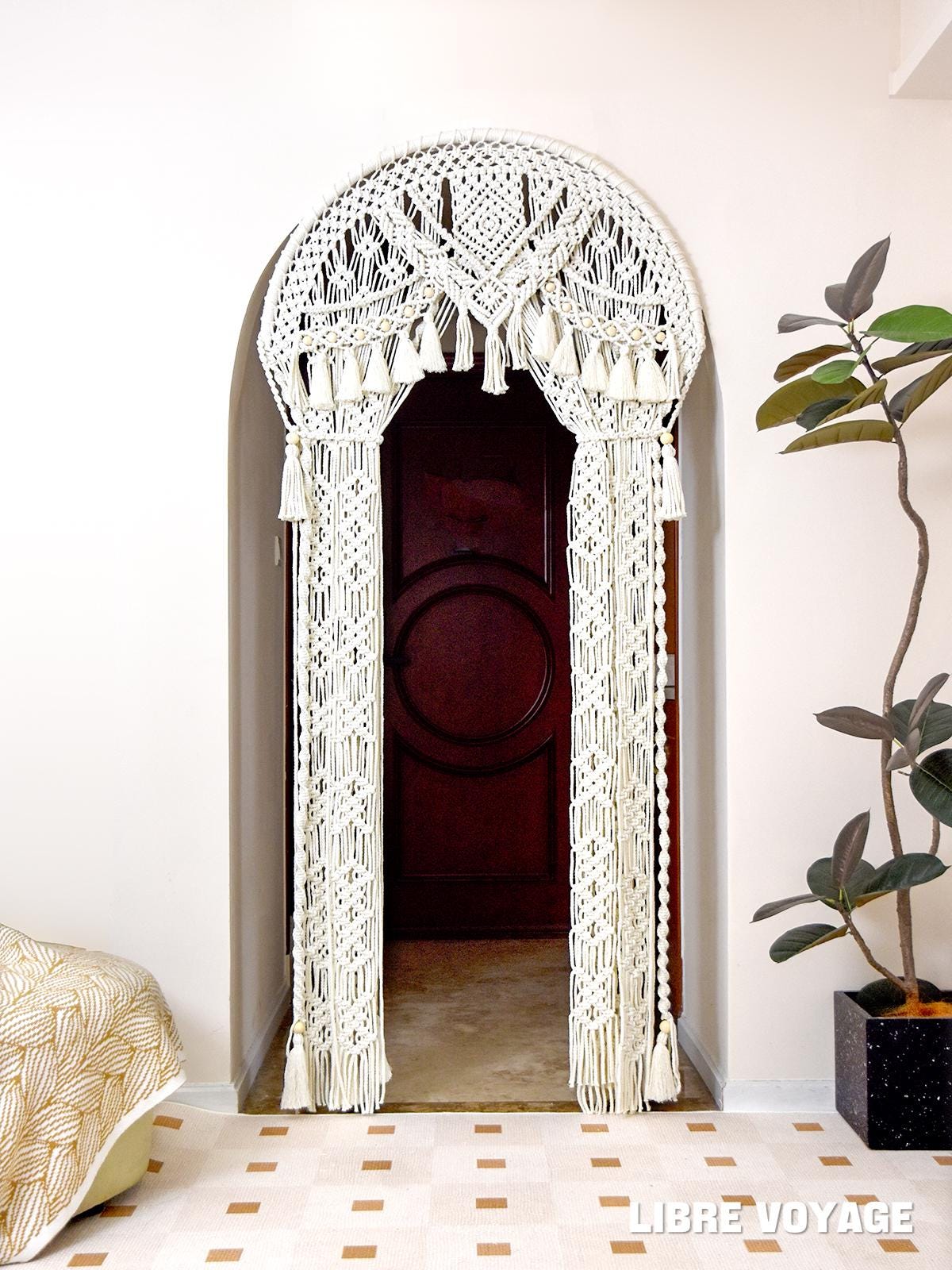 A cream cotton macramé curtain hanging over an arched doorway in a boho interior