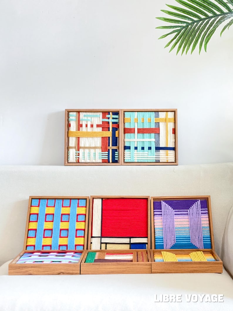 K&ouml;nnte beinhalten: Eine Sammlung von f&uuml;nf quadratischen Holzrahmen mit kunstvollen Wandbildern aus Garn. Die Designs zeigen Webmuster in leuchtenden Farben wie Rot, Gelb, Blau, Violett und Wei&szlig;. Der Text "LIBRE VOYAGE" ist in der unteren rechten Ecke zu sehen.