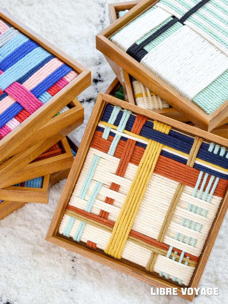 K&ouml;nnte beinhalten: Eine Sammlung quadratischer Holztabletts mit geflochtenen Seileins&auml;tzen in verschiedenen Farbmustern, darunter Blau, Rosa, Rot, Gelb und Creme. Der Text LIBRE VOYAGE ist in der unteren rechten Ecke des Bildes zu sehen.