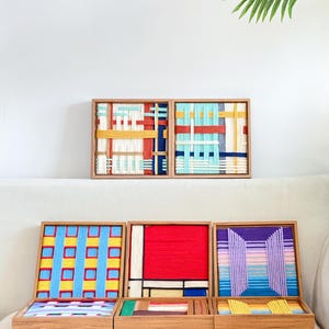 K&ouml;nnte beinhalten: Eine Sammlung von f&uuml;nf quadratischen Holzrahmen mit gewebter Garnkunst. Die Designs zeigen verschiedene geometrische Muster und Farbkombinationen, darunter rote, blaue, gelbe, wei&szlig;e, violette und t&uuml;rkisfarbene Garnstr&auml;nge in Gitter- und Blockanordnung.