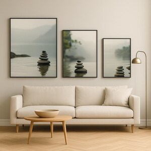 Peut inclure: Trois impressions d'art encadrées représentant des scènes d'eau sereines avec des pierres empilées. Les impressions, dans des cadres noirs, dépeignent un lac brumeux avec des rochers équilibrés, créant une atmosphère apaisante. L'œuvre est affichée au-dessus d'un canapé beige.
