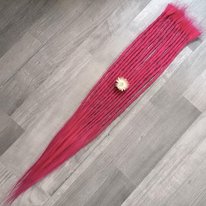 Könnte beinhalten: Ein Bündel leuchtend pinkfarbener Dreadlocks, diagonal angeordnet. Eine kleine, weiß-gelbe Blume liegt auf den Dreadlocks. Die Dreadlocks liegen auf einer grauen Holzoberfläche.
