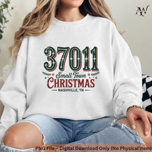 May include: White sweatshirt with the text "37011 Small Town Christmas Nashville, TN" in green and red. The design includes a postal code, festive greenery, and stars, perfect for holiday wear.
