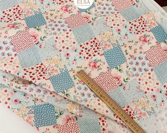 May include: Patchwork fabric with a floral pattern in red, pink, and yellow on a light blue and cream background. The fabric is arranged in a grid of squares, some with polka dots. A wooden ruler is placed on the fabric.