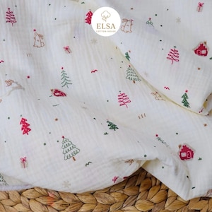 May include: Off-white muslin fabric with a Christmas-themed pattern. The design includes red and green embroidered Christmas trees, houses, and gift boxes, along with small dots and a few reindeer and rabbits. The fabric is slightly wrinkled.